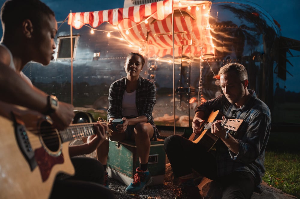 Friends playing with a pair of acoustic guitars in a camp fire